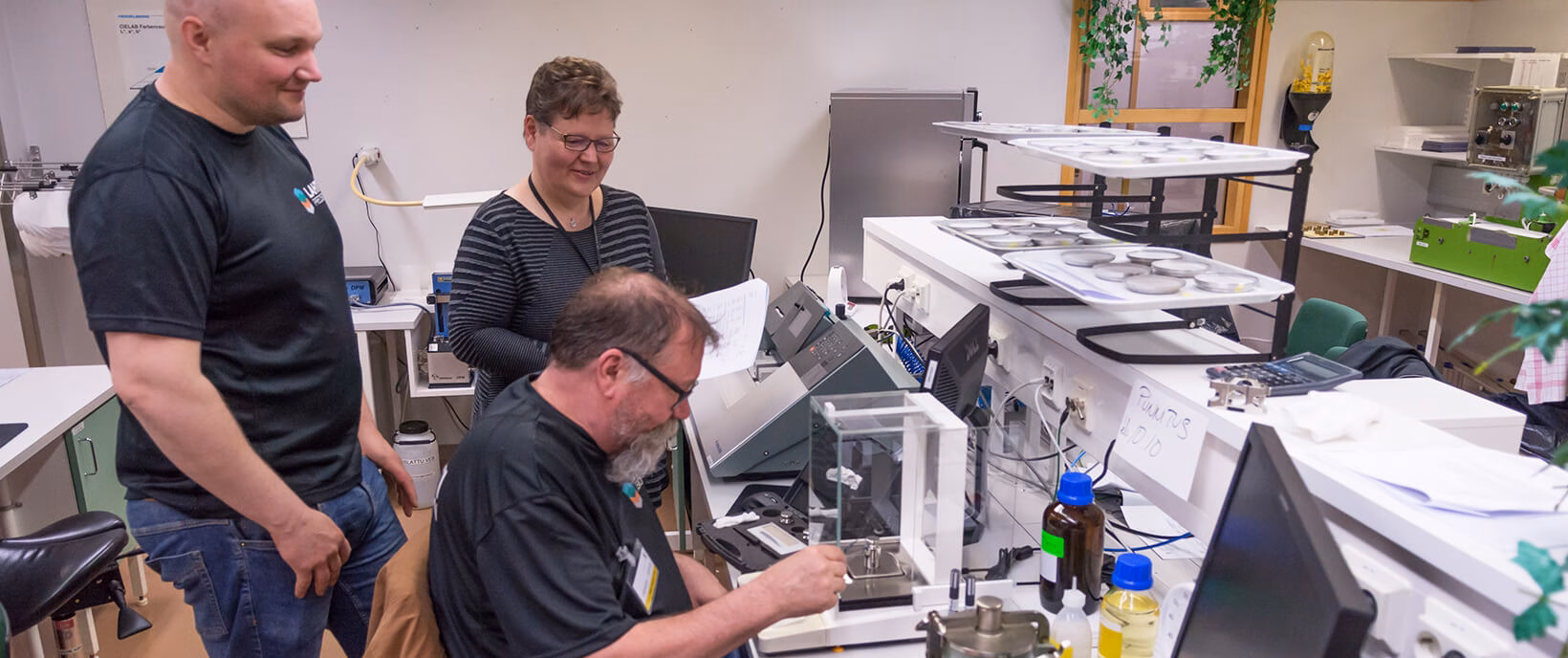Three employees performing calibration work with precision weighing equipment