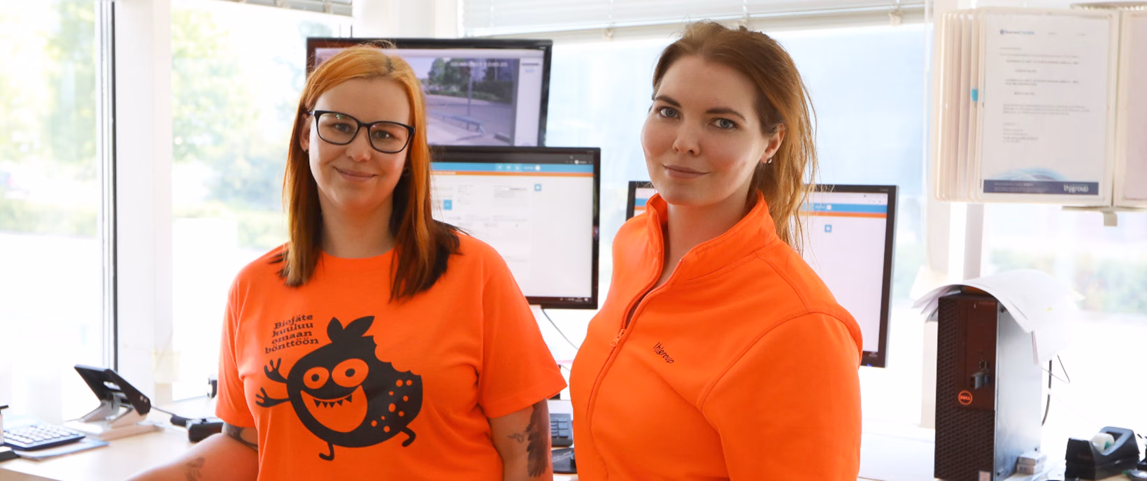 Two weighing operators in an office with computer screens and a window in the background