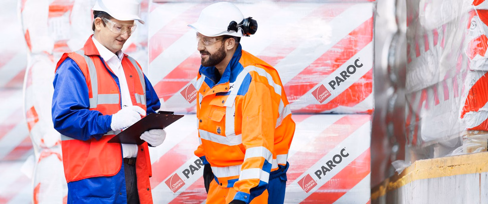 Two workers in safety gear on a work site with mineral wool insulation bales in the background