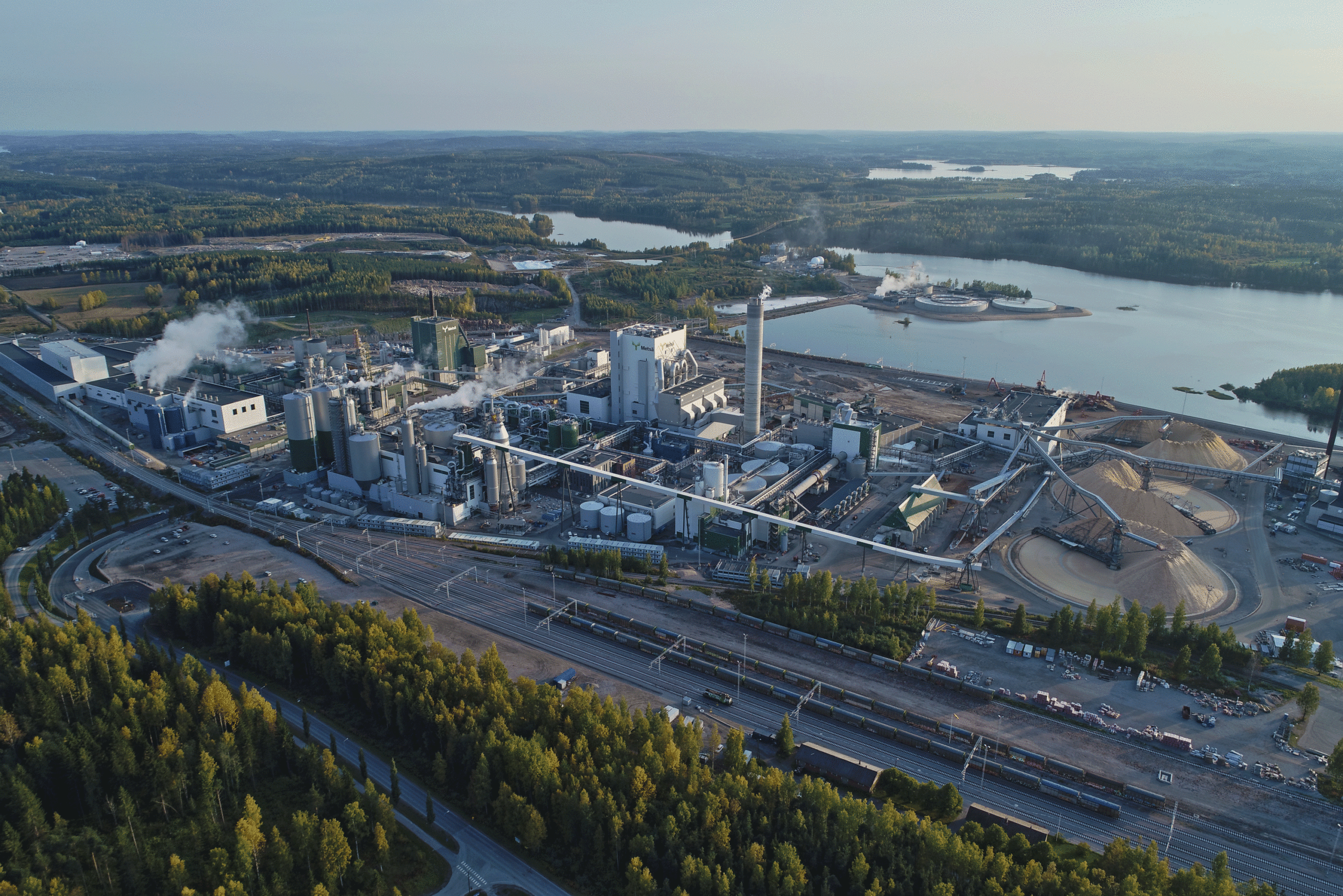 An aerial view of a bioproduct mill with a lake and forest in the background