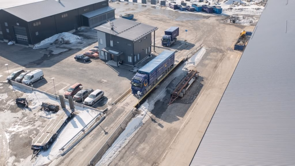 An aerial view of a truck on a truck scale with a recycling center in the background
