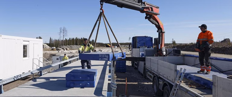 Autovaa’an varmennus, jossa kuorma-autonosturi nostaa tarkastuspainoja vaa’alle työntekijöiden valvonnassa