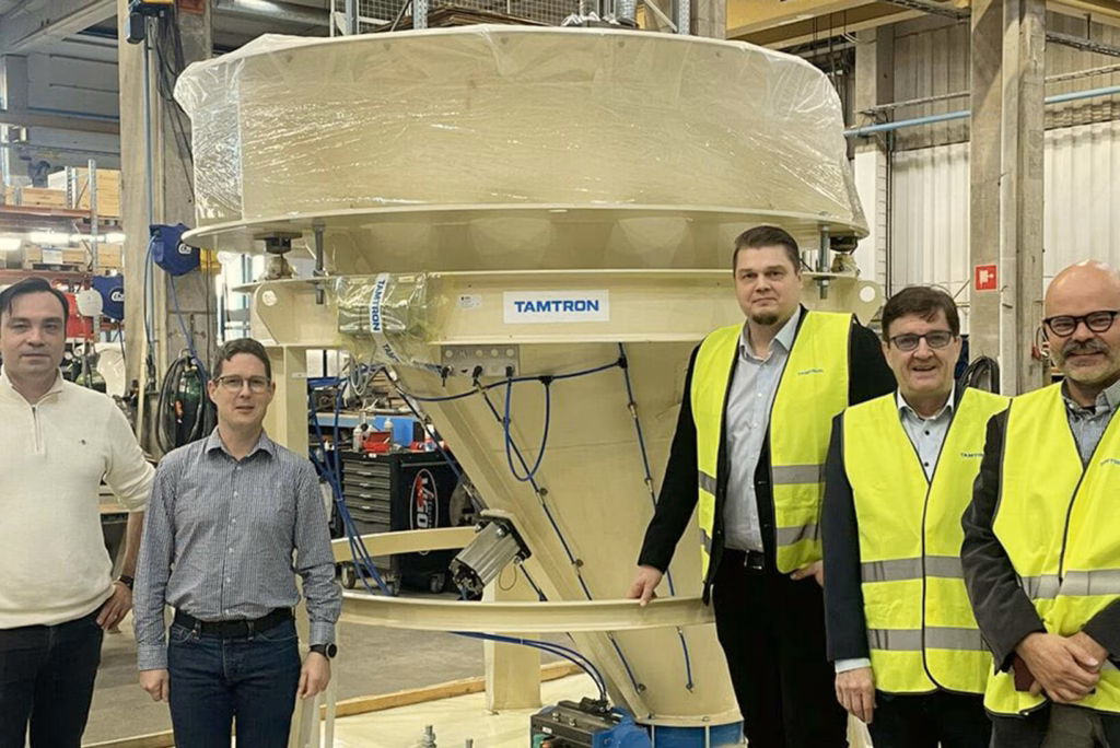 Skupina lidí stojí vedle systému pro manipulaci s materiálem Tamtron v hale