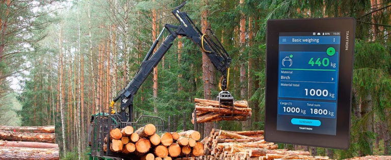 Metsäkoneen kuormain nostaa tukkeja metsässä ja vieressä näkyy tabletti, jossa One Timber -käyttöliittymä.