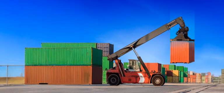 Red reach stacker lifting a shipping container at a port yard