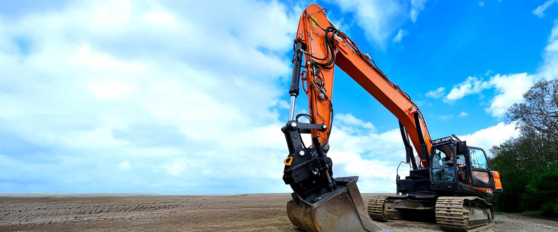 Orange hydraulic excavator on a flat sandy worksite
