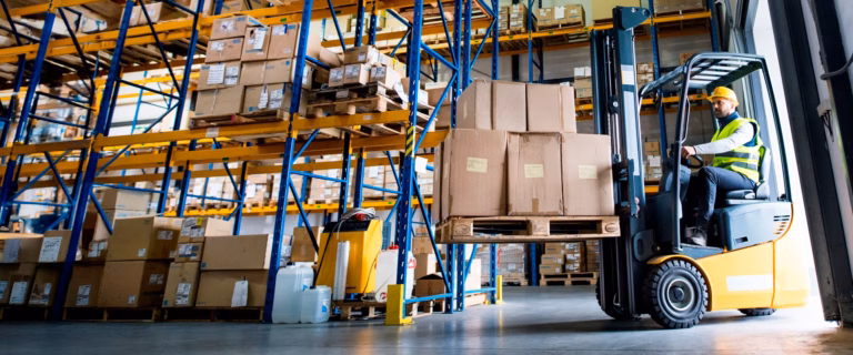 Worker operating a yellow forklift carrying boxed pallets in a warehouse