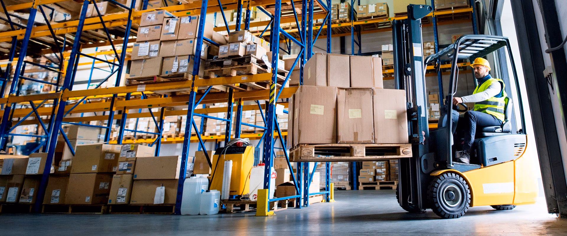 Worker operating a yellow forklift carrying boxed pallets in a warehouse