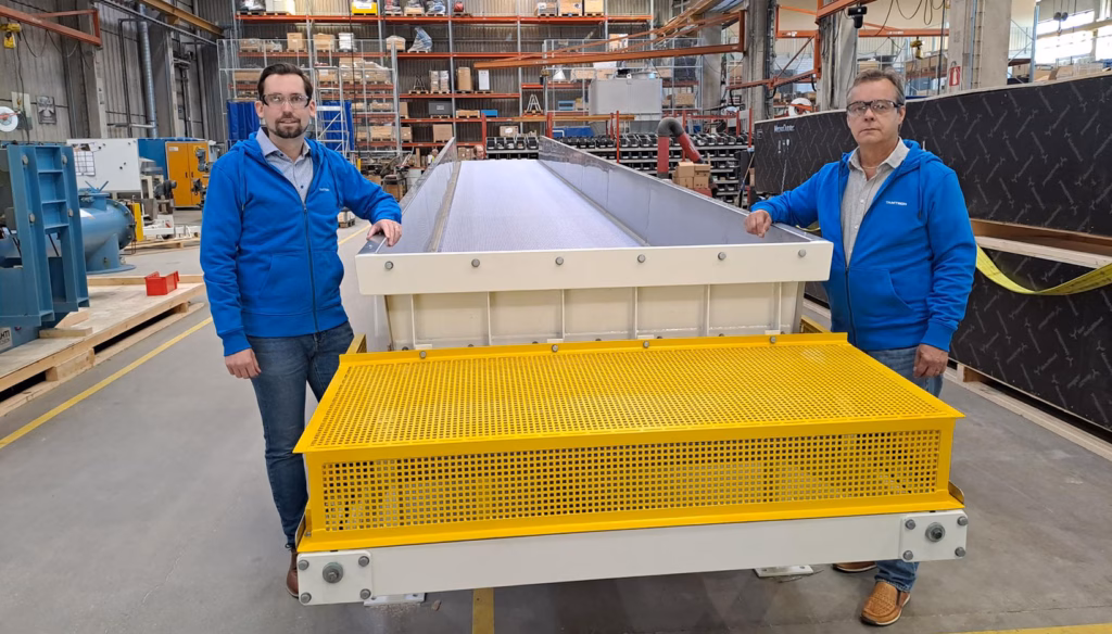 Two men standing with a Tamtron broke conveyor in a warehouse