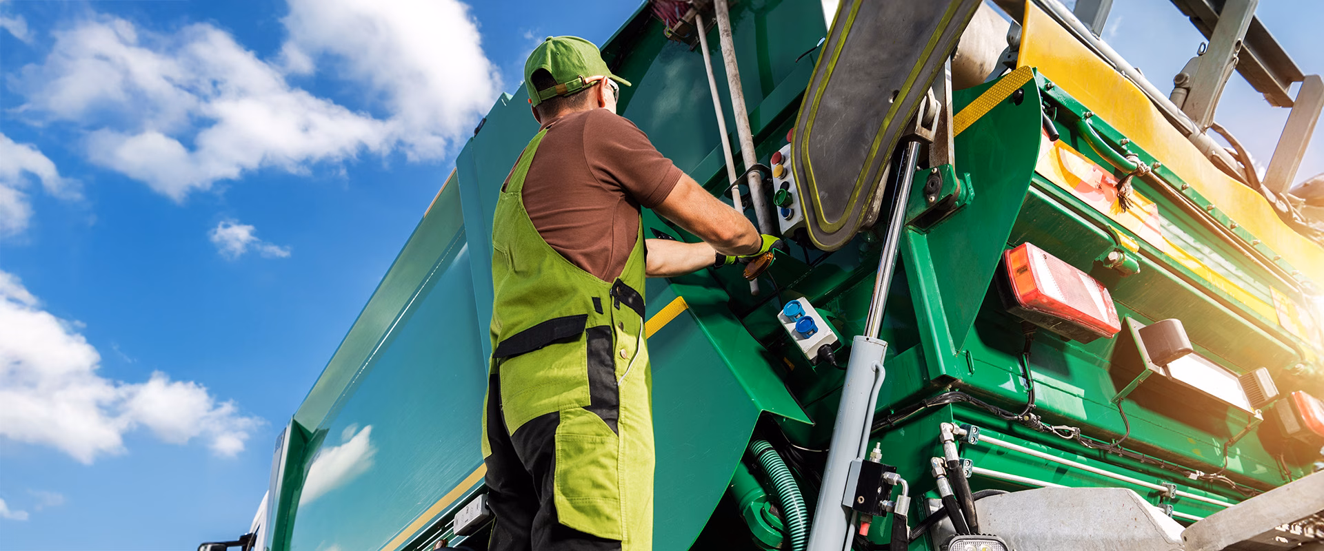 Worker in high-visibility vest operating the rear controls of a green truck body