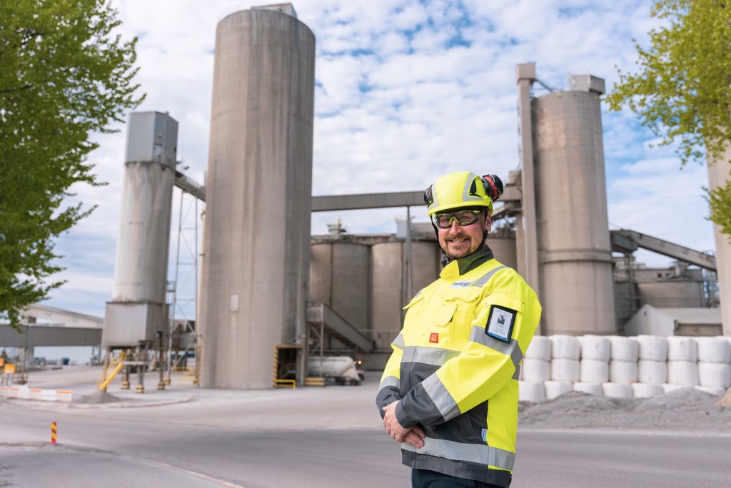 A man wearing high visibility clothing, a safety helmet and protective glasses standing in front of a concrete plant