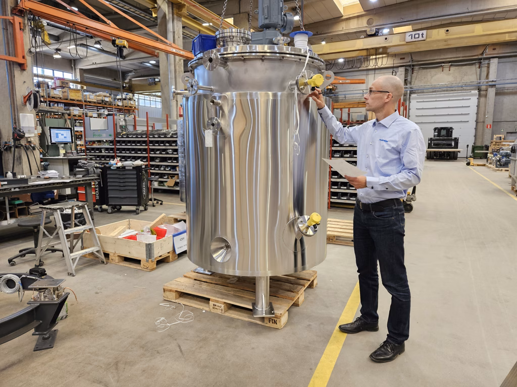 Man next to a large steel mixing tank in a warehouse
