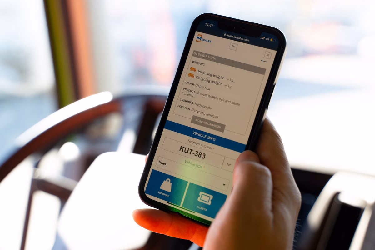 Hand holding a smartphone showing the mScales interface inside a truck cabin