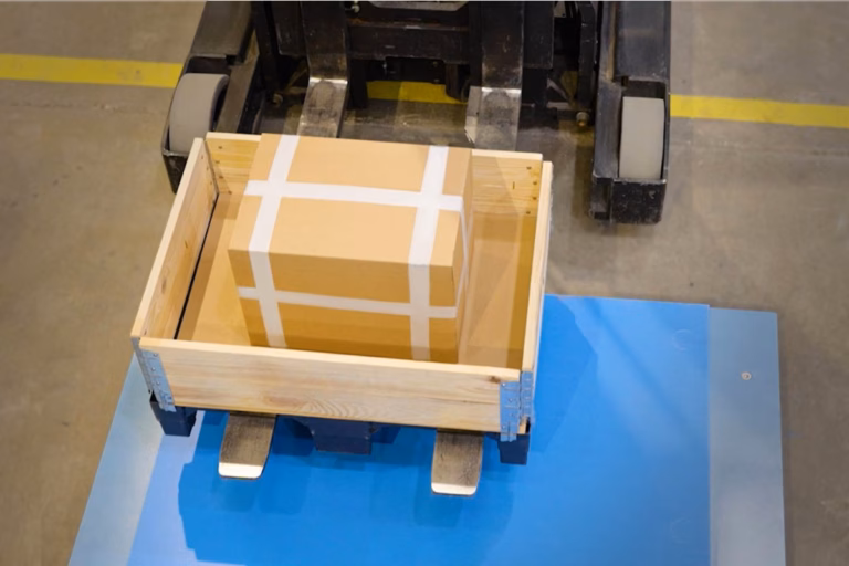 Forklift placing a wooden pallet with a cardboard box onto an industrial floor scale for weighing