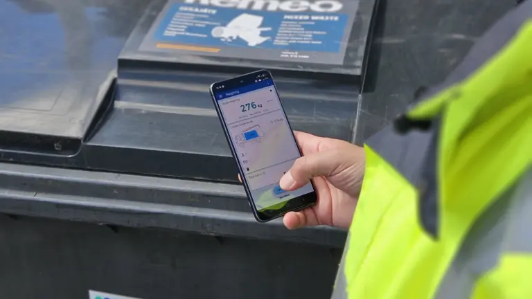 Worker in hi-vis vest holds mobile phone with Tamtron Weighing Application